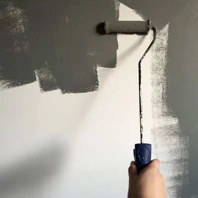 Painter applying gray paint with a roller to an interior wall. Stock photograph.